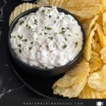 Clam dip in a dark bowl surrounded by kettle potato chips.