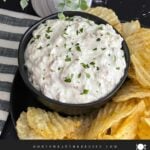 Clam dip in a dark bowl surrounded by kettle potato chips.