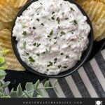 Clam dip in a dark bowl surrounded by kettle potato chips.