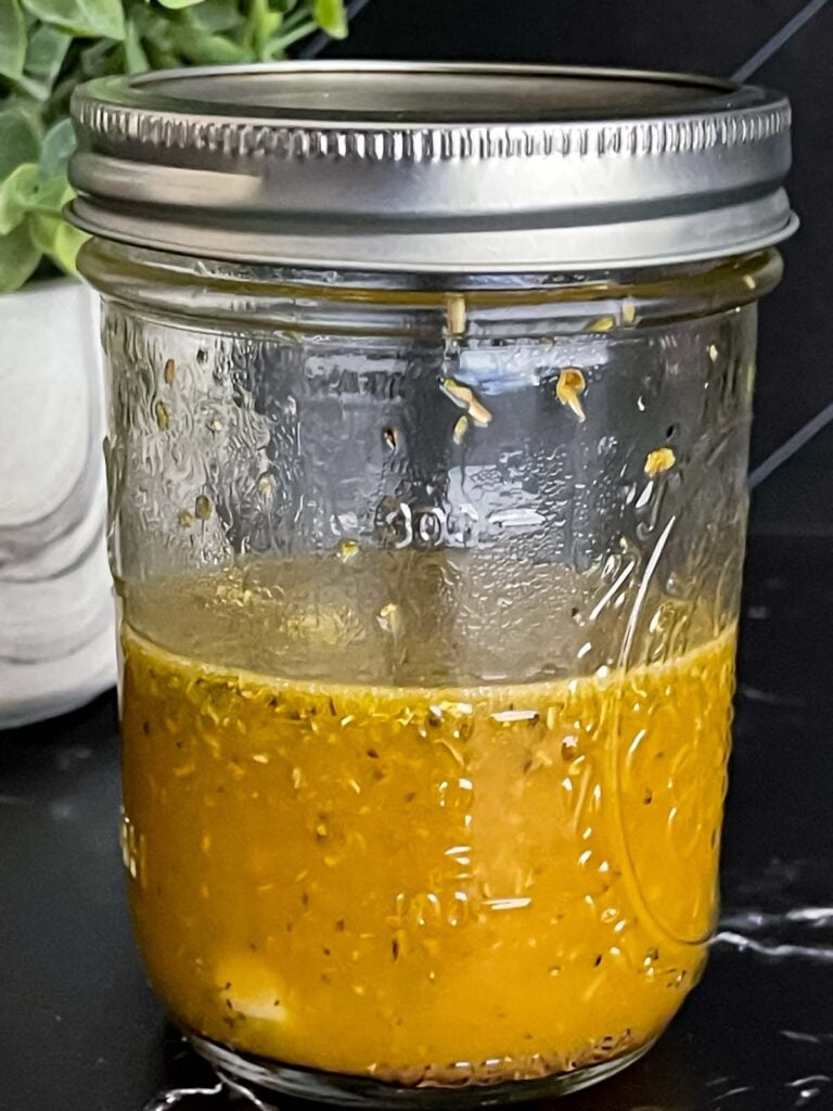 Greek dressing in a glass jar on a dark surface.