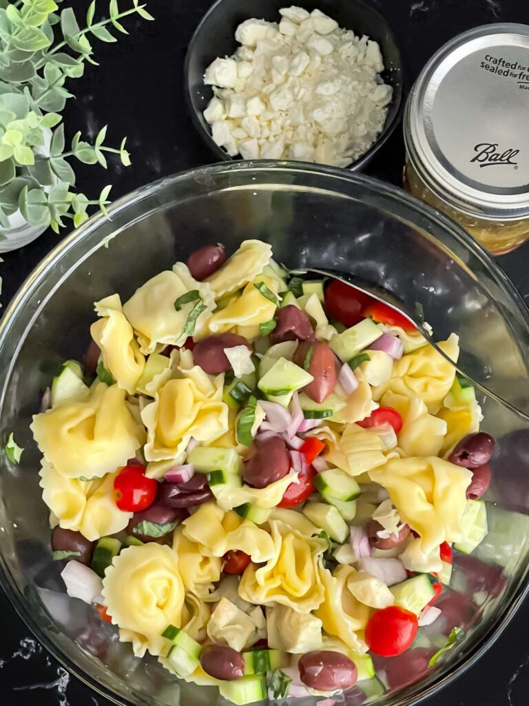 Vegetables tossed with the tortellini in a glass mixing bowl.