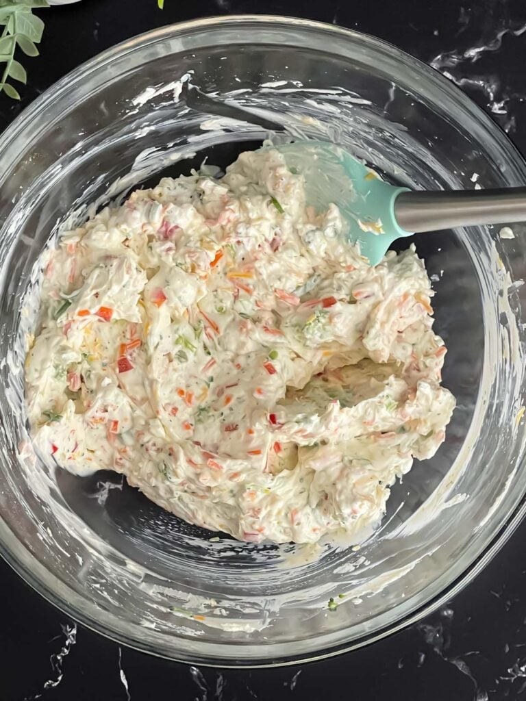 Vegetable cream cheese mixture combined in a glass mixing bowl for the veggie tortilla roll ups.