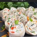 Veggie tortilla roll ups lined up on a square dark plate garnished with diced green onions and shredded carrots.