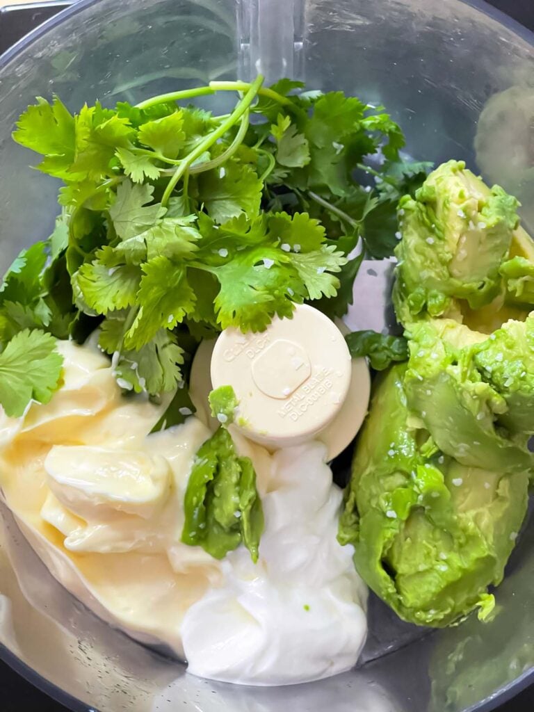 Avocado crema sauce ingredients in a food processor bowl.