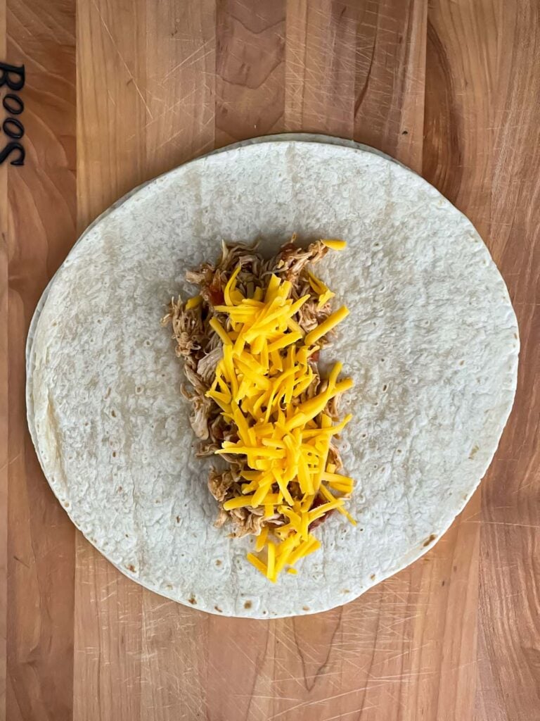Shredded Mexican chicken and shredded sharp cheddar cheese in the middle of a burrito size tortilla.