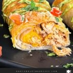 Baked chicken chimichangas on a dark oval platter garnished with avocado crema, diced tomatoes and cilantro.