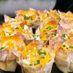 Buffalo chicken wontons garnished with chives and blue cheese crumbles on a cutting board.