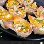 Buffalo chicken wontons garnished with chives and blue cheese crumbles on a dark plate.