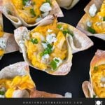 Buffalo chicken wontons garnished with chives and blue cheese crumbles on a dark plate.
