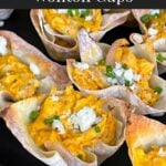 Buffalo chicken wontons garnished with chives and blue cheese crumbles on a dark plate.
