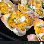 Buffalo chicken wontons garnished with chives and blue cheese crumbles on a dark plate.
