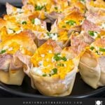 Buffalo chicken wontons garnished with chives and blue cheese crumbles on a dark plate.