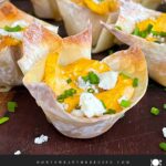 Buffalo chicken wontons garnished with chives and blue cheese crumbles on a dark plate.