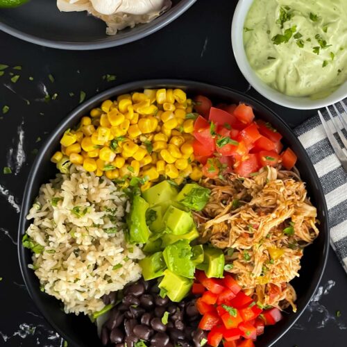 A chicken burrito bowl with an avocado sauce on a dark background.