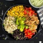 A chicken burrito bowl with an avocado sauce on a dark background.