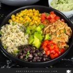 A chicken burrito bowl with an avocado sauce on a dark background.