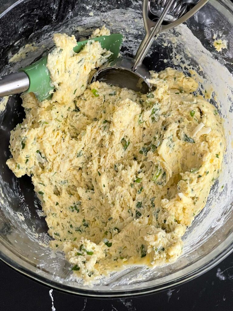 Herb and cheese muffin batter mixed in a large glass bowl.