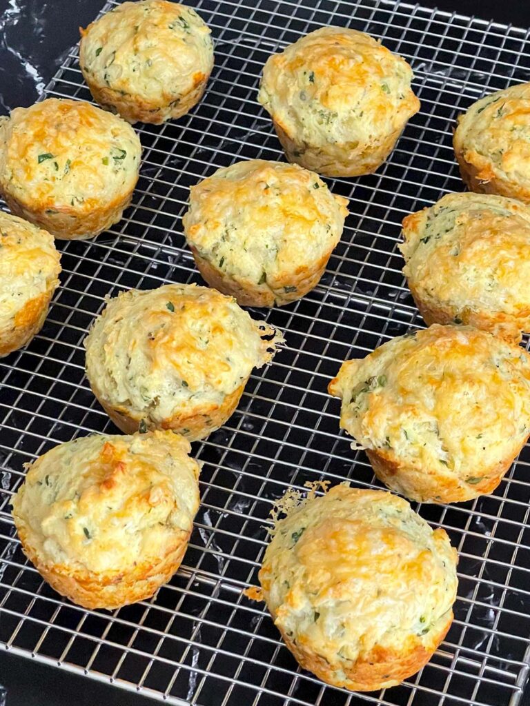 Herb and cheese muffins on a wire rack on a dark surface.