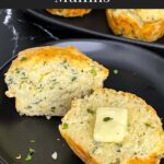Herb and cheese muffin cut in half topped with butter on a dark plate.