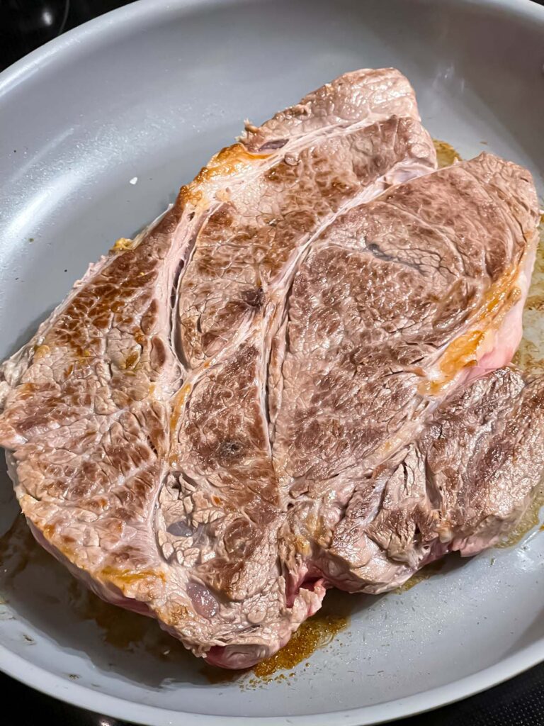 Beef chuck roast seared in a skillet.
