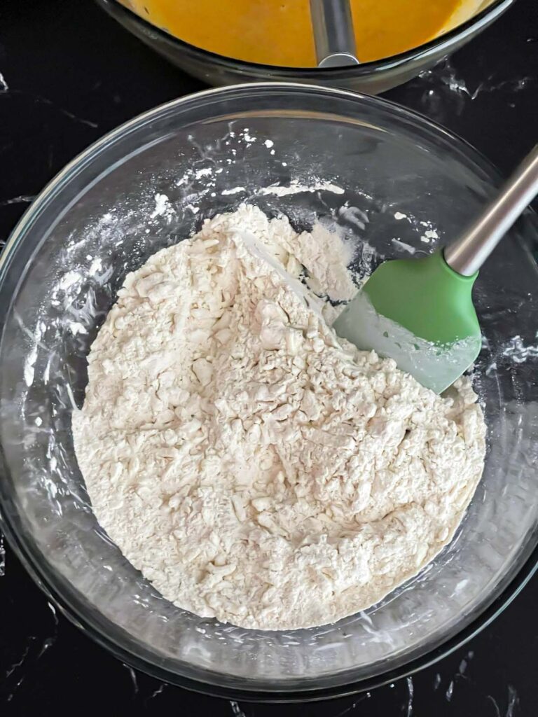 Shredded frozen butter added to the dry ingredients in a glass mixing bowl.