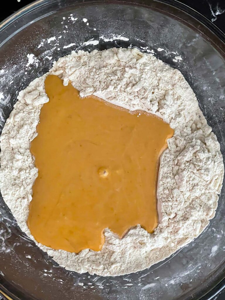 Pumpkin scone wet batter poured into the center of the dry ingredients in a glass bowl.