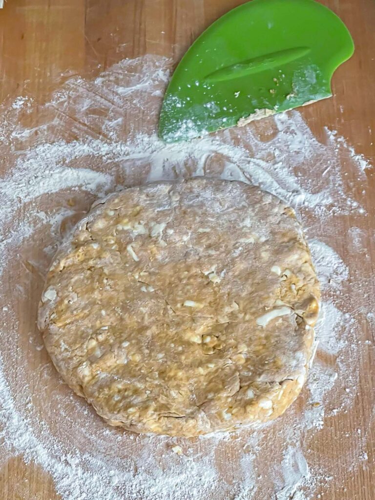 Pumpkin scone dough shaped into a 1-inch thick circle on a floured wooden board.