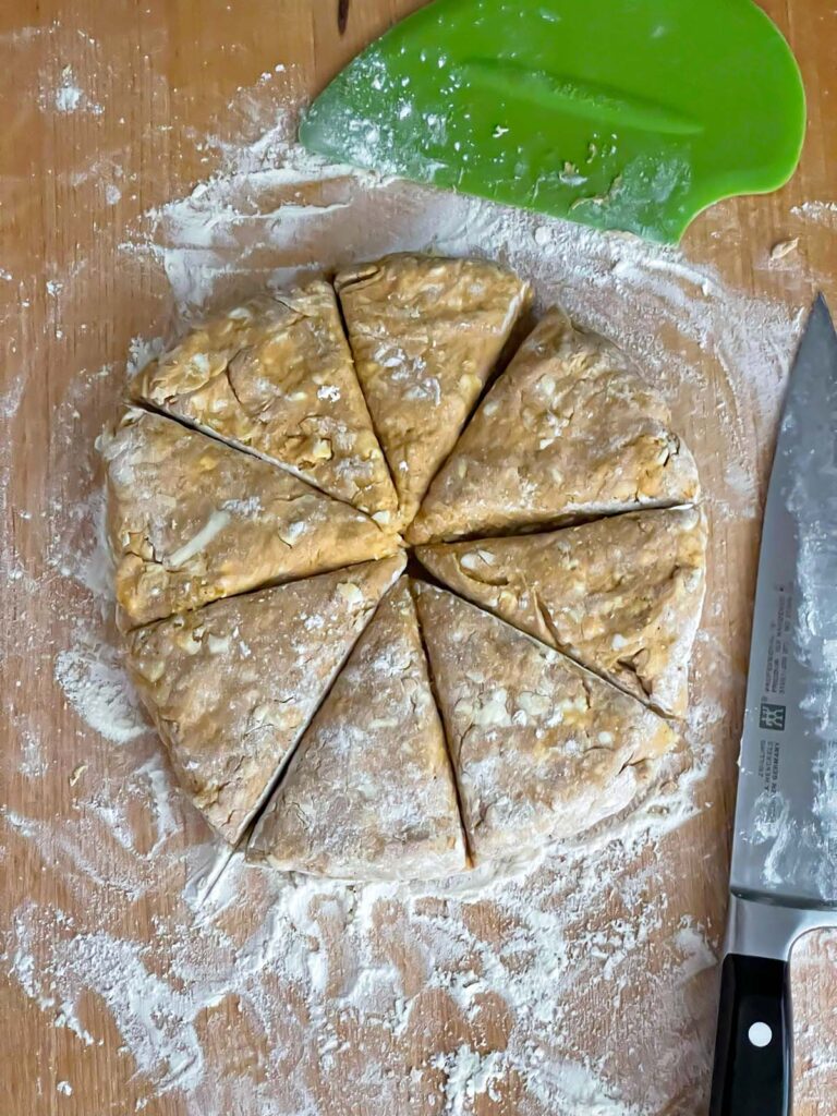 Pumpkin scone dough cut into eight equal pieces on a wooden board.