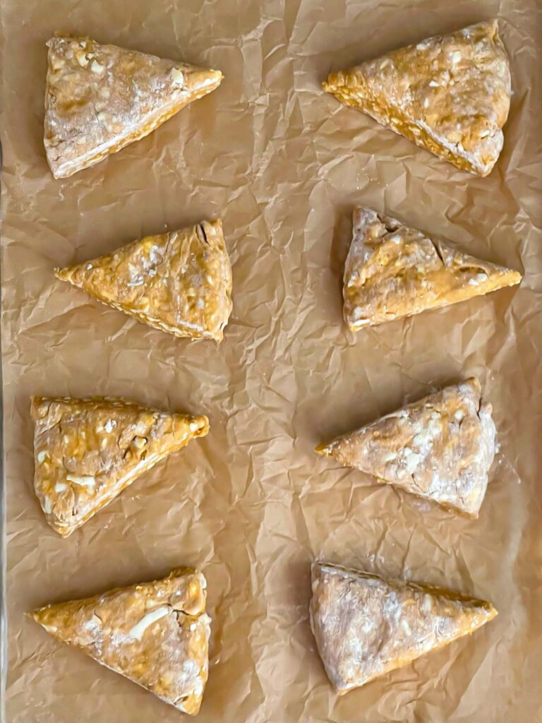 Unbaked pumpkin scones on a parchment paper lined baking sheet.