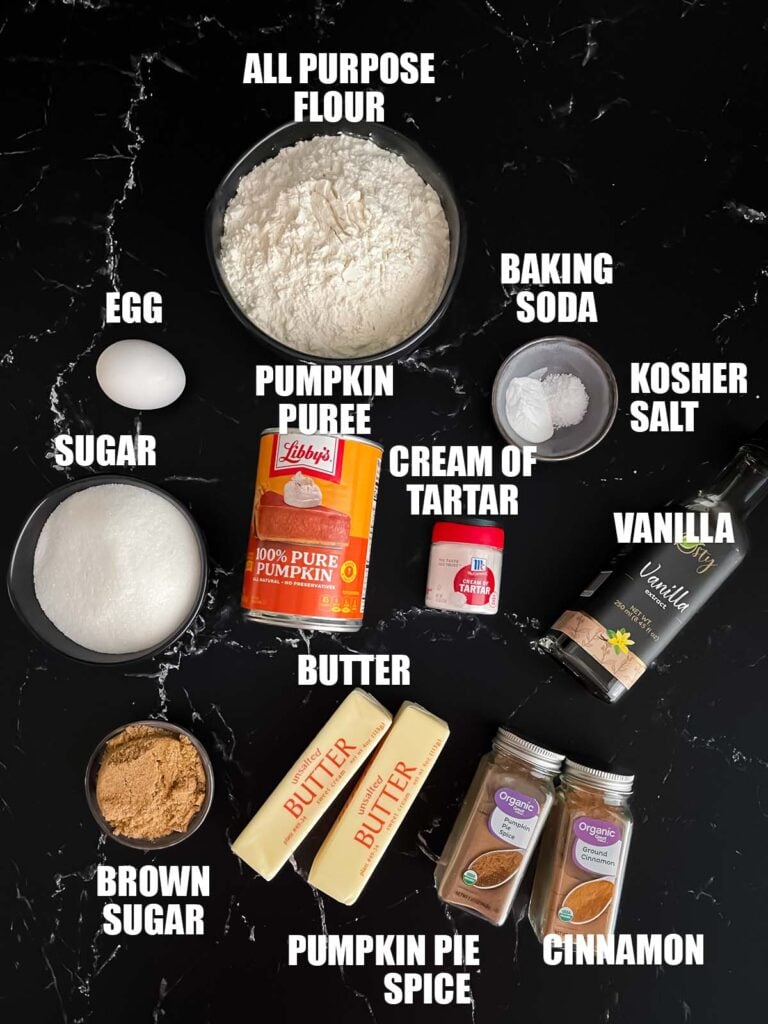 Pumpkin Snickerdoodles recipe ingredients on a dark surface.