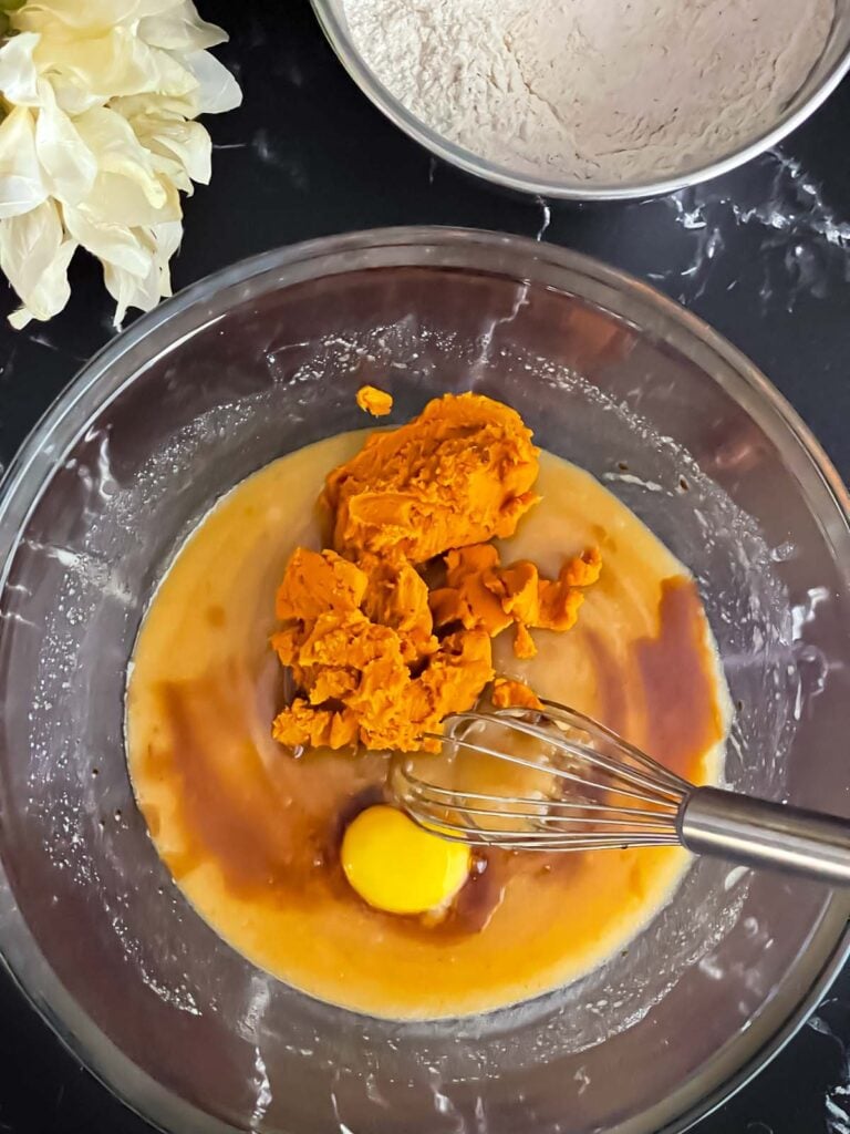 Blotted pumpkin, egg, and vanilla added to the wet ingredients in a glass bowl.