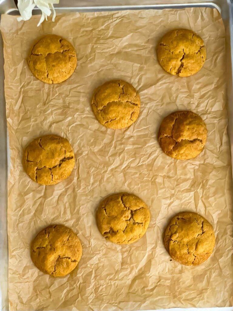 Baked pumpkin snickerdoodle cookies on a parchment paper lined cookie sheet.