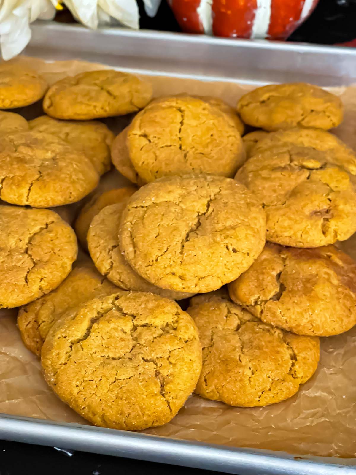 Pumpkin snickerdoodles stacked on a parchment paper lined baking sheet.