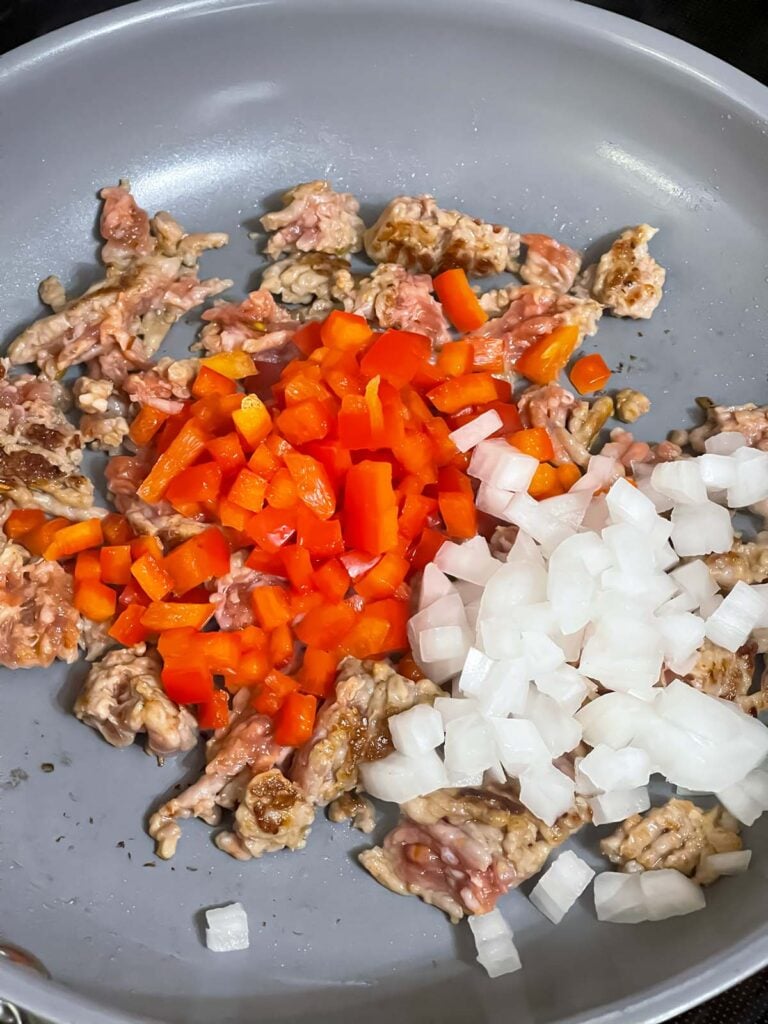 Sausage cooking in a skillet with red bell pepper and onions.
