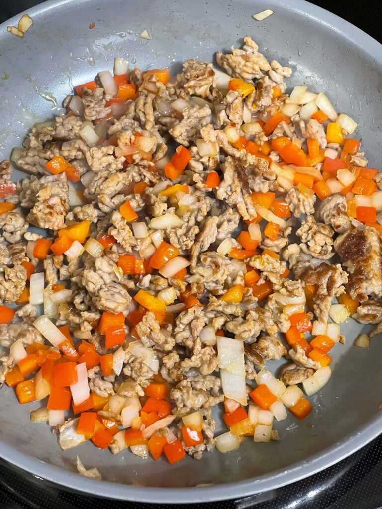 Sausage cooking in a skillet with red bell pepper and onions.