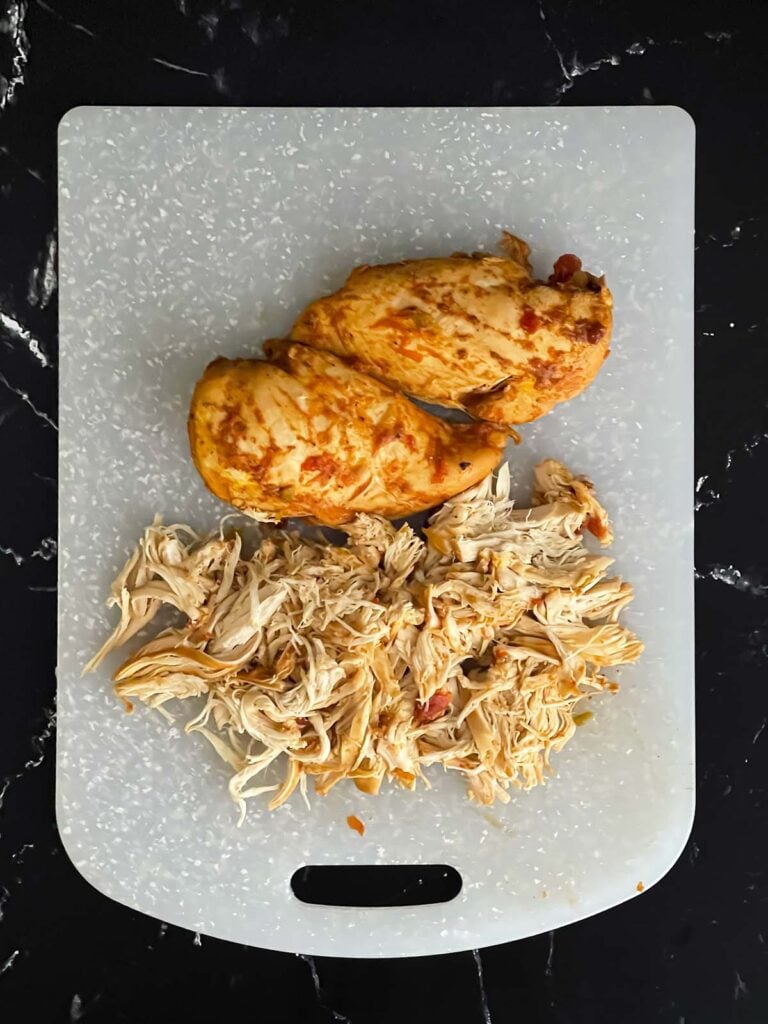 Shredded Mexican chicken on a plastic cutting board on a dark surface.