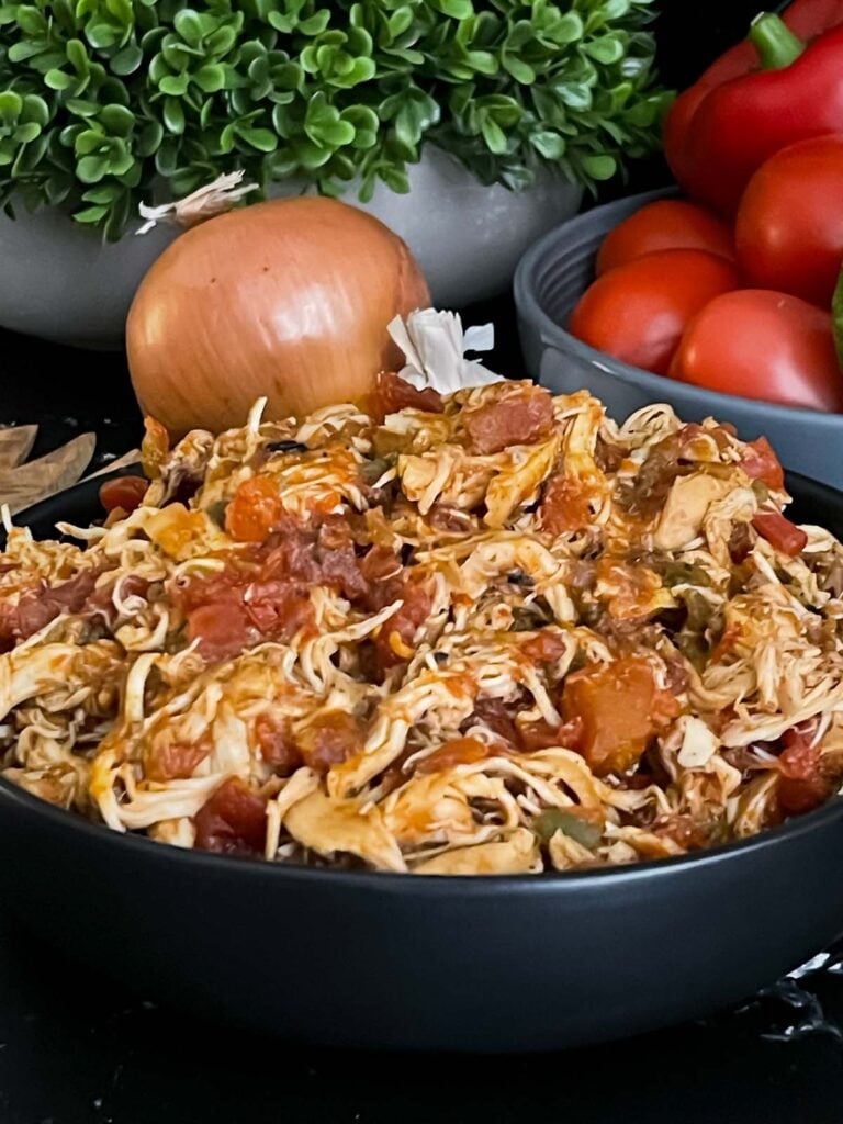 Slow cooker Mexican chicken in a dark bowl on a dark surface.