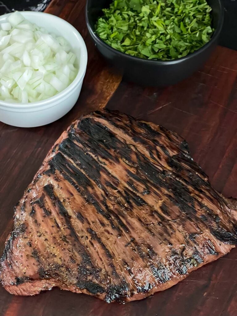 Grilled flank steak on a cutting board with some onions and cilantro.