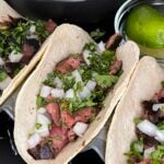 Flank steak street tacos with rice and garnish on a dark background.