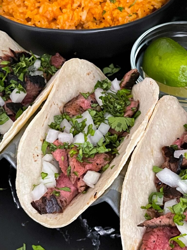 Flank steak street tacos with rice and garnish on a dark background.