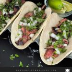 Flank steak street tacos with rice, chips, and garnish on a dark background.