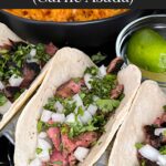 Flank steak street tacos with rice, chips, and garnish on a dark background.