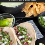 Flank steak street tacos with rice, chips, and garnish on a dark background.