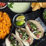 Flank steak street tacos with rice, chips, and garnish on a dark background.