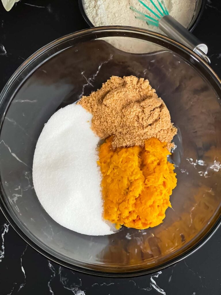 Sugars and mashed sweet potato in a glass mixing bowl on a dark surface.