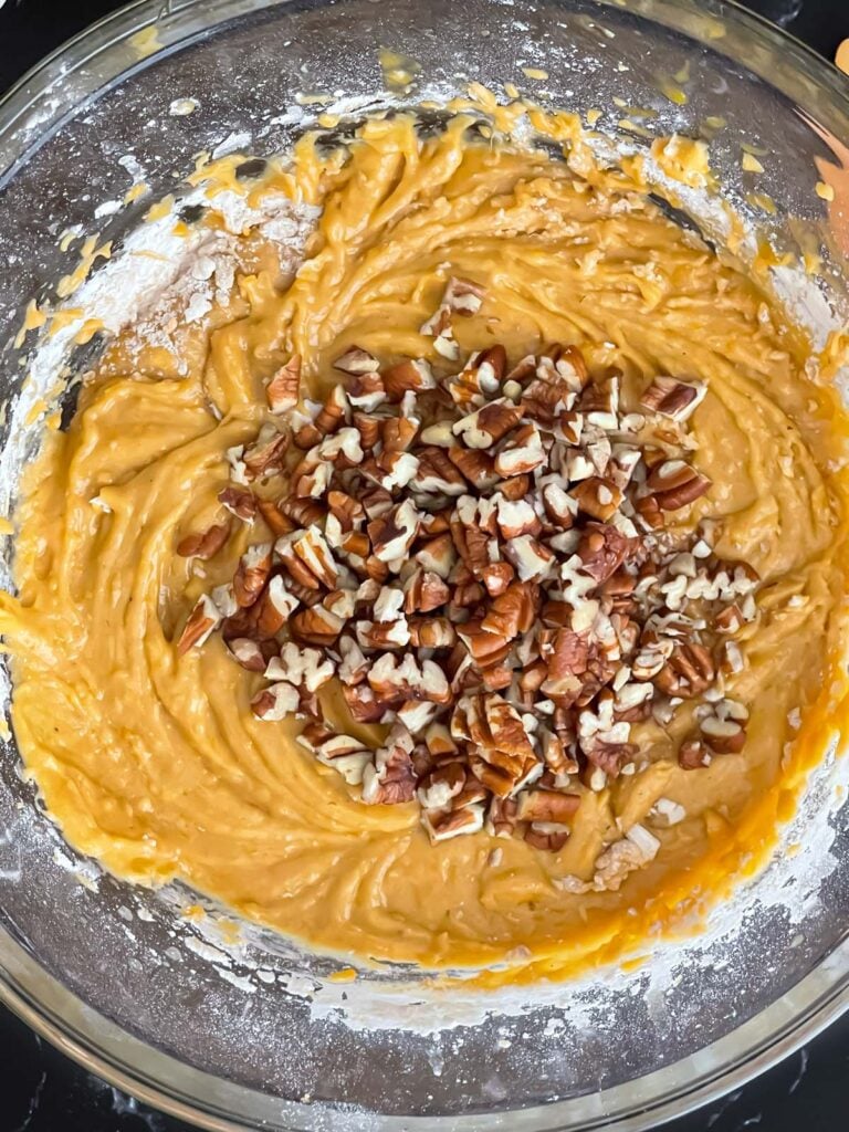 Pecans added to sweet potato bread batter in a glass bowl.