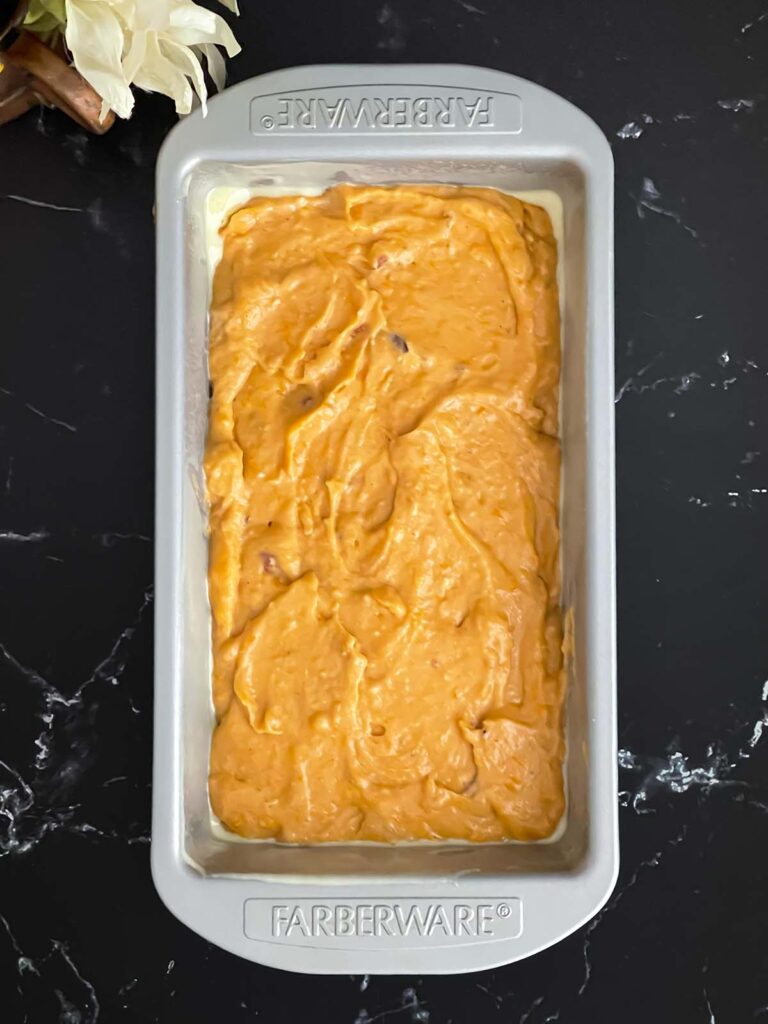 Sweet potato bread batter in a greased loaf pan on a dark surface.