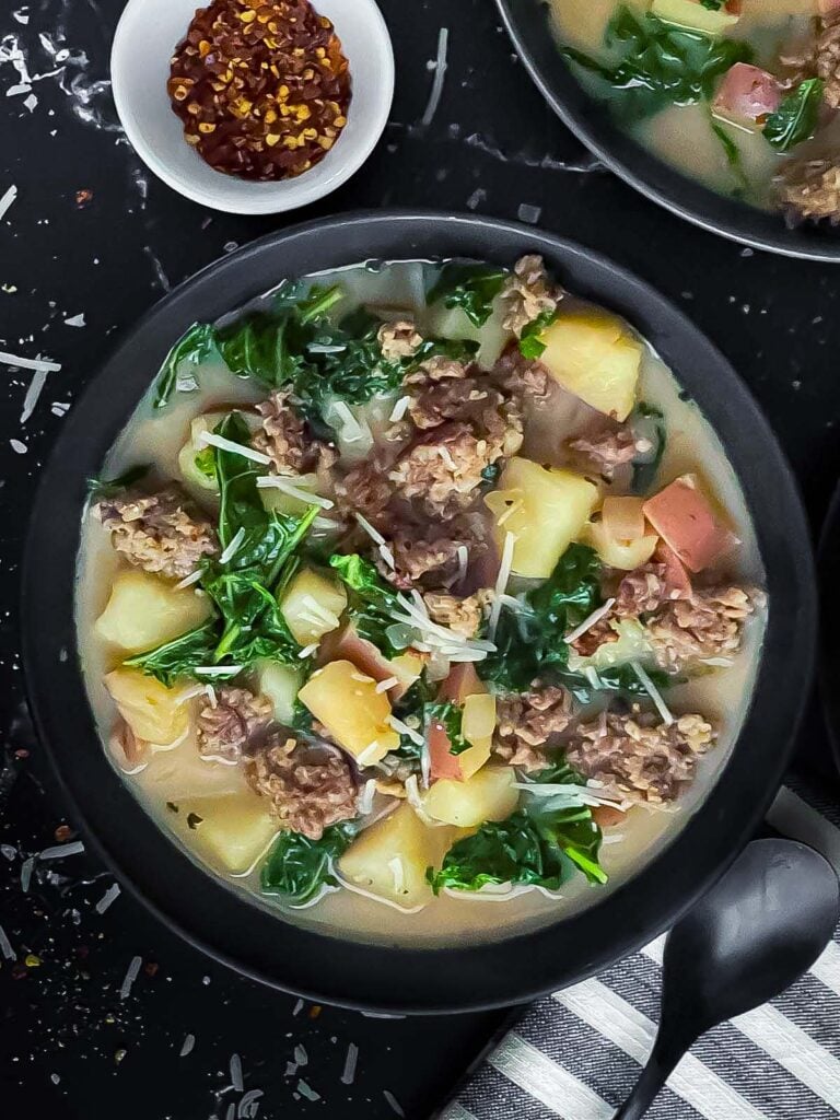 Sausage, potato and kale soup (Zuppa Toscana) in dark bowls on a dark surface.