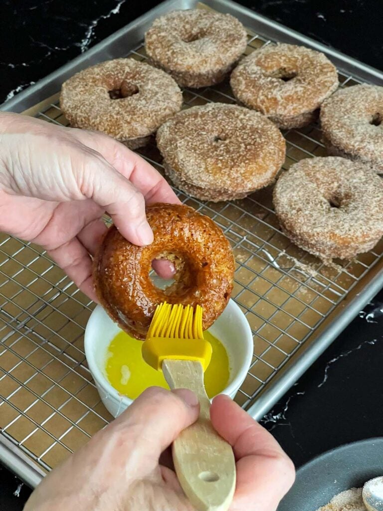 Melted butter being brushed over a baked apple cider donut.