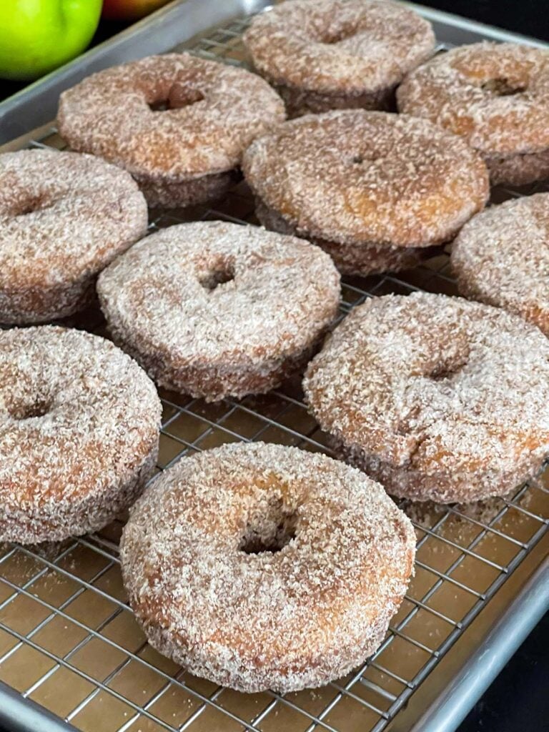 Baked apple cider donuts on a wire rack over a parchment paper lined baking pan.